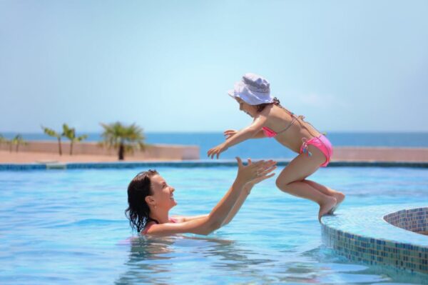 beautiful woman catches little girl jumping in pool against sea